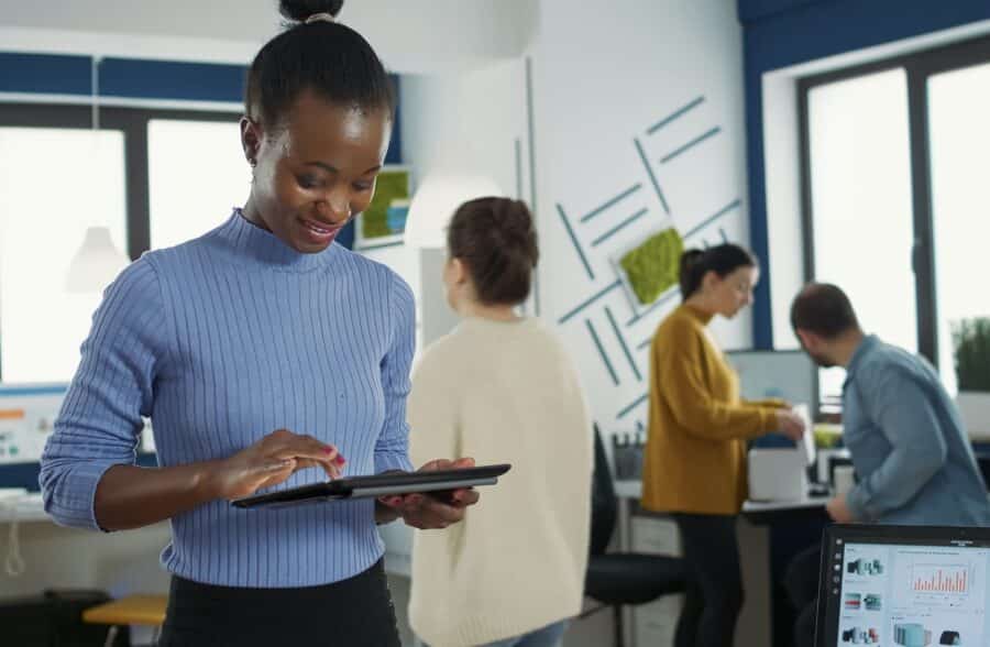 Portrait of african american woman standing in busy office picking up tablet with business erp